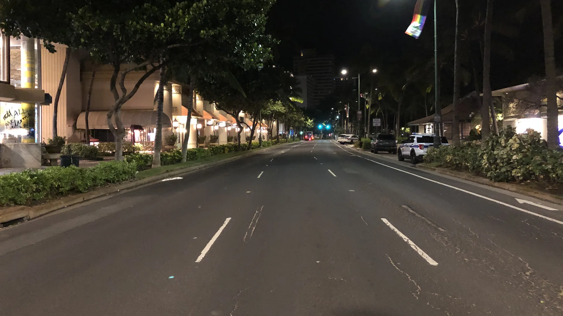 Kalākaua Avenue w Waikiki nocą, bez ruchu, palmy i podświetlone witryny sklepów po obu stronach ulicy